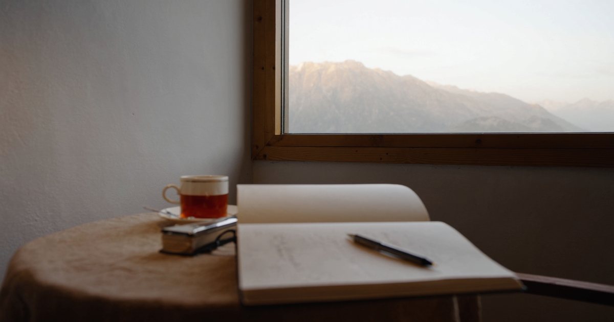 Aufgeschlagenes Notizbuch mit Stift an einem Fenster mit Bergblick